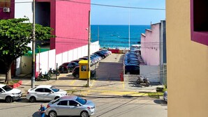 Vista da rua com um edifício em primeiro plano, um estacionamento com carros e uma vista desobstruída do oceano ao fundo.