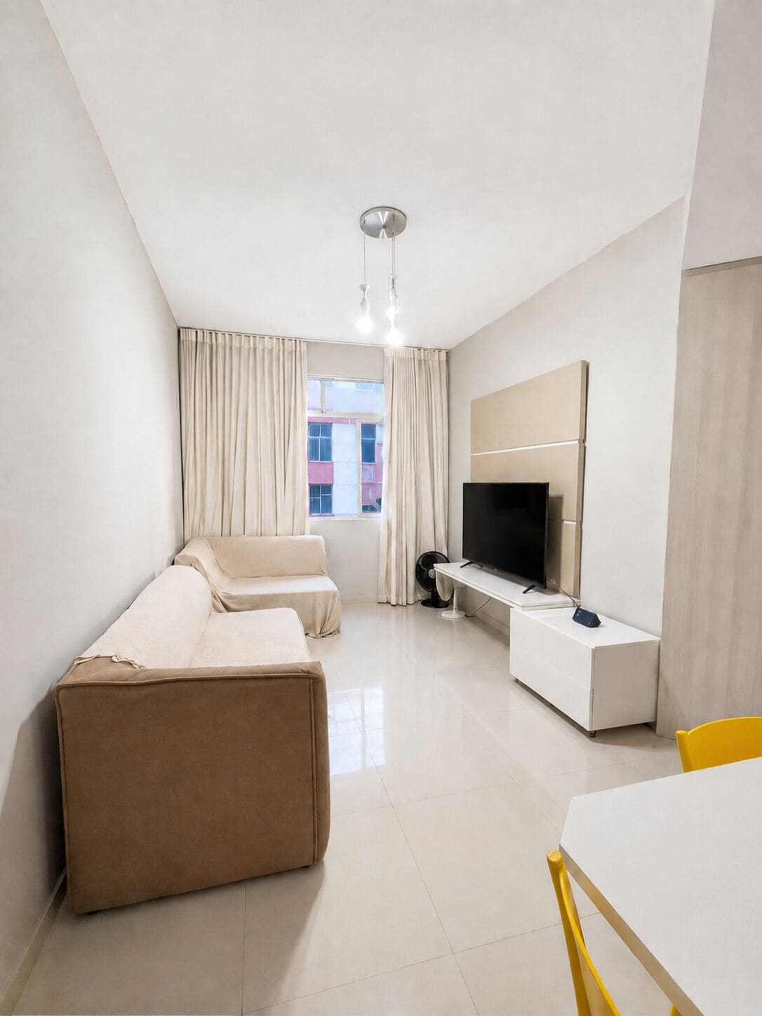 A modern hotel room with a sofa, a TV, a small table, and a window with curtains.