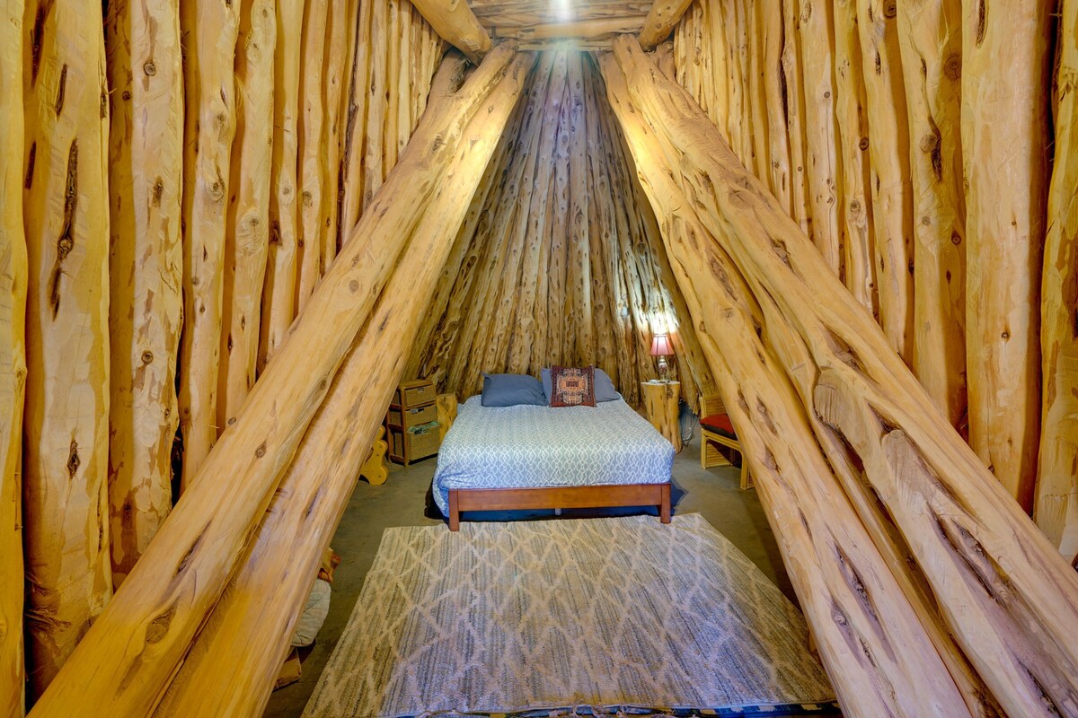 A tent-like room with a bed centered, wooden walls, and a small table with a lamp.