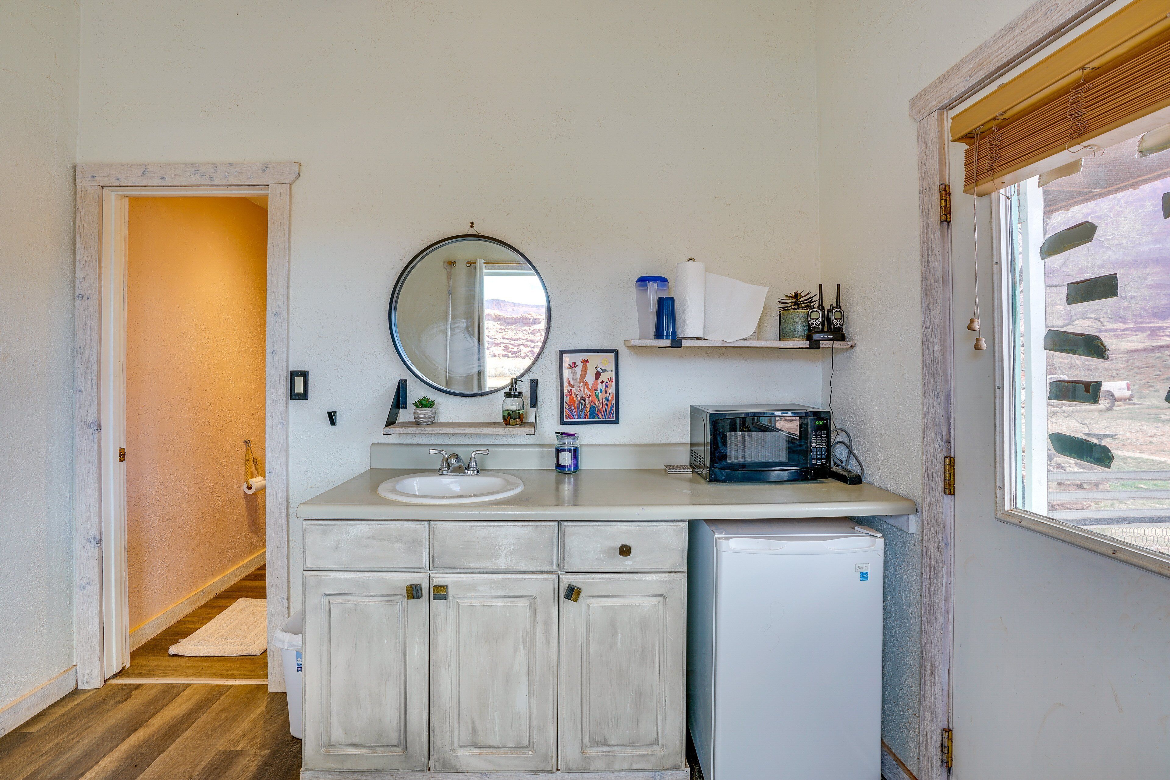 A compact bathroom with a sink, mirror, and a microwave.