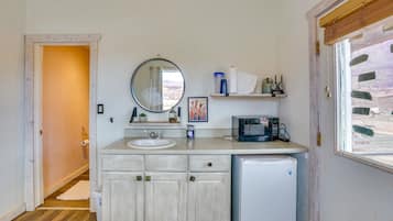 A compact bathroom with a sink, mirror, and a microwave.