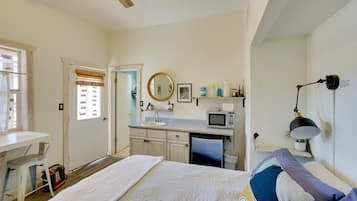 A bedroom with a bed, a desk, a chair, a window, and a ceiling fan.