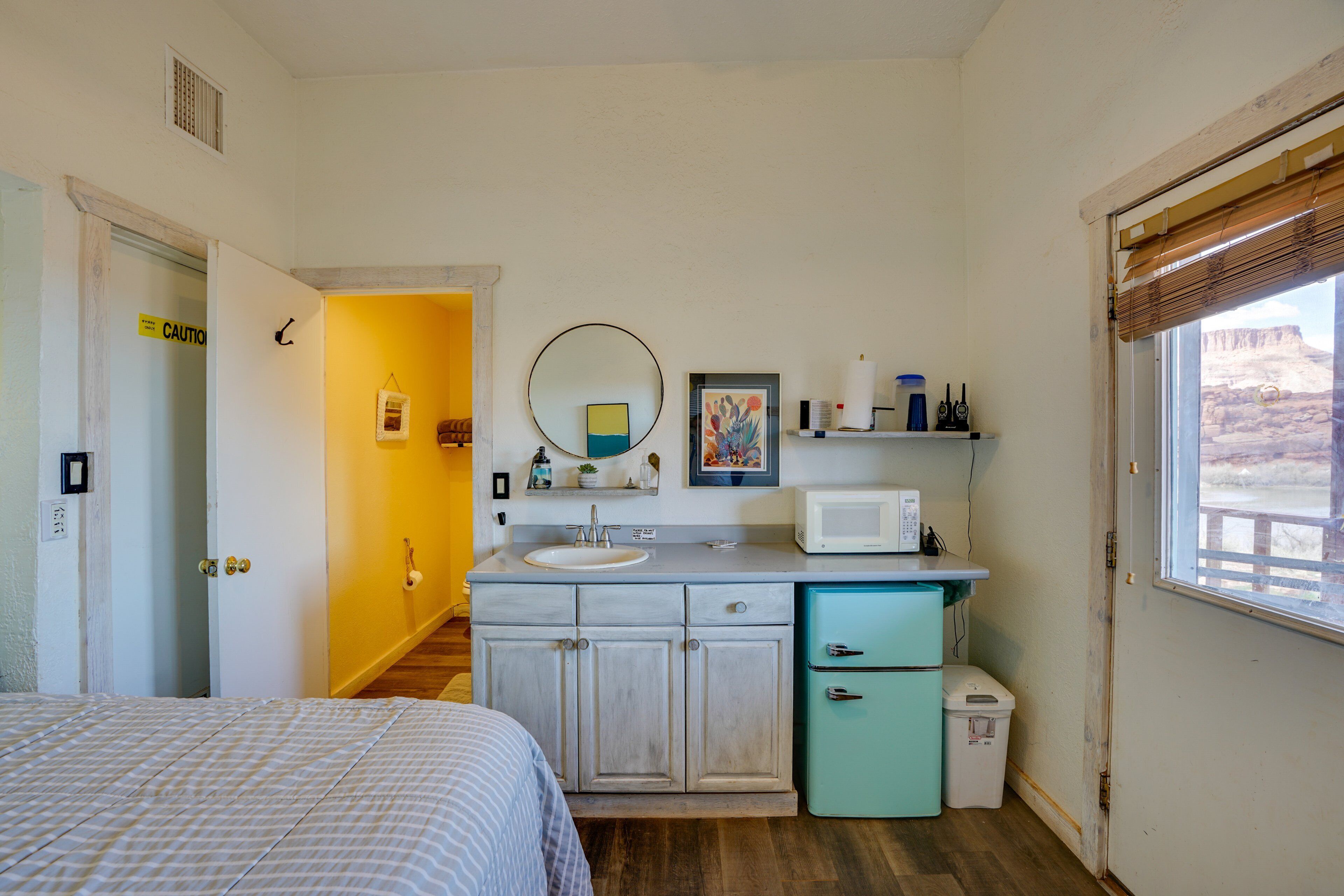A compact bedroom with a bed, a bathroom with a sink and mirror, and a window with a view.