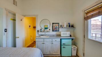 A compact bedroom with a bed, a bathroom with a sink and mirror, and a window with a view.