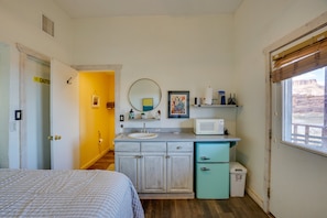 A compact bedroom with a bed, a bathroom with a sink and mirror, and a window with a view.