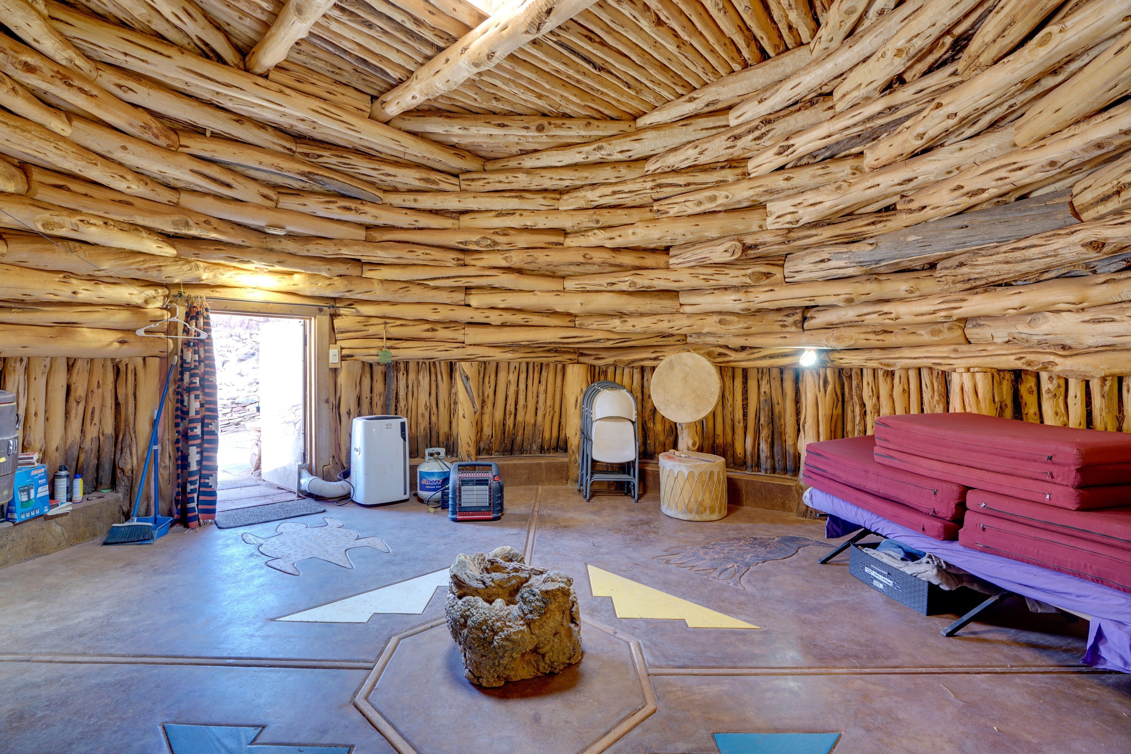 A rustic interior with a wooden ceiling, a bed with red bedding, a chair, and a small table with a decorative item.