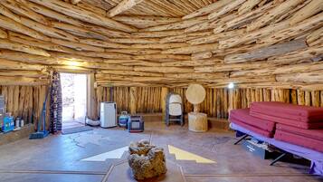 A rustic interior with a wooden ceiling, a bed with red bedding, a chair, and a small table with a decorative item.
