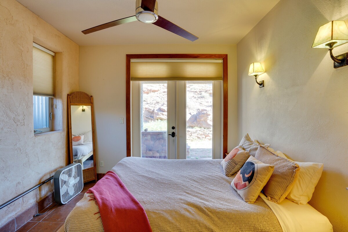 A bedroom with a bed, a ceiling fan, a window with blinds, a mirror, and a wall-mounted lamp.