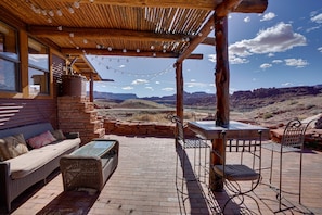 An outdoor patio with a wooden pergola, string lights, a brick fireplace, a sofa, and a table with chairs. - Base Camp Adventure Lodge (Moab)