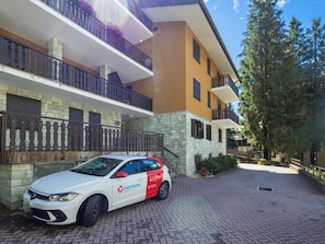 A white car parked in front of a building with a stone facade and balconies. - Ai Pascoli by Interhome (Madesimo)