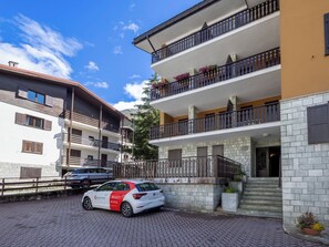 A multi-story residential building with balconies, a car parked in front, and a paved driveway. - Ai Pascoli by Interhome (Madesimo)