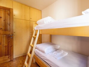Un lit superposé avec une literie blanche, une échelle en bois et une armoire en bois avec une porte.