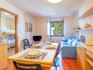 A compact room with a dining table set for two, a sofa, a TV, and a window with a view of trees. - Ai Pascoli by Interhome (Madesimo)