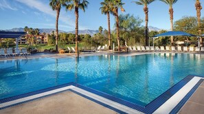 A swimming pool with lounge chairs and palm trees, surrounded by a landscaped area with a view of mountains. - Coachella 2028 and 2029 Rentals!  Both Weekends Available (Palm Desert)