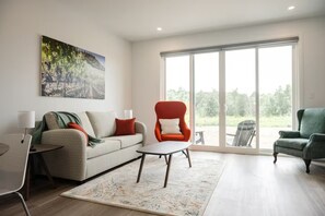 A modern living room with a sofa, two armchairs, a coffee table, and a large window. - New Vineyard Cottage in Niagara Wine Country | 1BR | Pet Friendly (Lincoln)