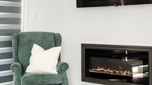 Un salon avec un fauteuil vert, un téléviseur à écran plat fixé au mur et une cheminée.