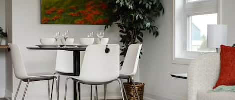 A dining area with a table set for four, white chairs, and a large painting on the wall.
