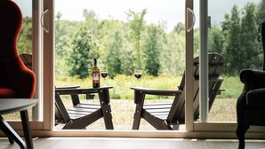 Une pièce dotée d’une porte-fenêtre coulissante donnant sur un espace extérieur aménagé avec deux tables et des chaises, une bouteille de vin et deux verres.