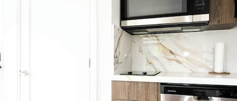 A kitchen with a microwave, dishwasher, and marble countertop.