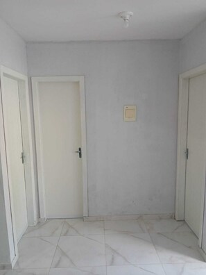 Ein Zimmer mit weiß gefliestem Boden, zwei weißen Türen und einer Deckenleuchte.