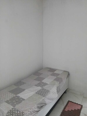 Ein kleiner, schmaler Raum mit einem Einzelbett, das mit einer Patchworkdecke bezogen ist.