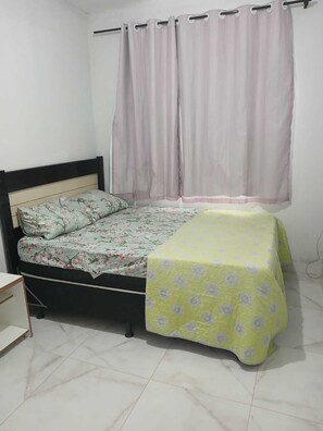 A single bed with a floral bedspread, a bedside table, and a curtain. - House 5 minutes from the Mozambique dunes trail (Florianópolis)