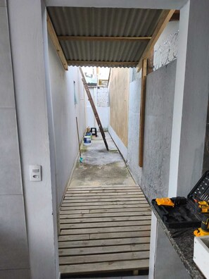 A narrow corridor with a wooden floor, a metal roof, and a concrete wall on the right. - House 5 minutes from the Mozambique dunes trail (Florianópolis)