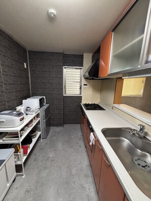 A compact kitchen with a gas stove, a sink, and a window with blinds. - Straight from KIX! Easy Access to Kyoto & Nara / Spacious House for Families & Groups (大阪市西成区千本北)
