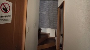 Un pasillo estrecho con una puerta de madera a la izquierda y una escalera que lleva a una habitación con cortina estampada.