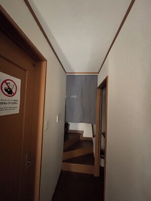 A narrow hallway with a wooden door on the left and a staircase leading to a room with a patterned curtain. - Straight from KIX! Easy Access to Kyoto & Nara / Spacious House for Families & Groups (大阪市西成区千本北)