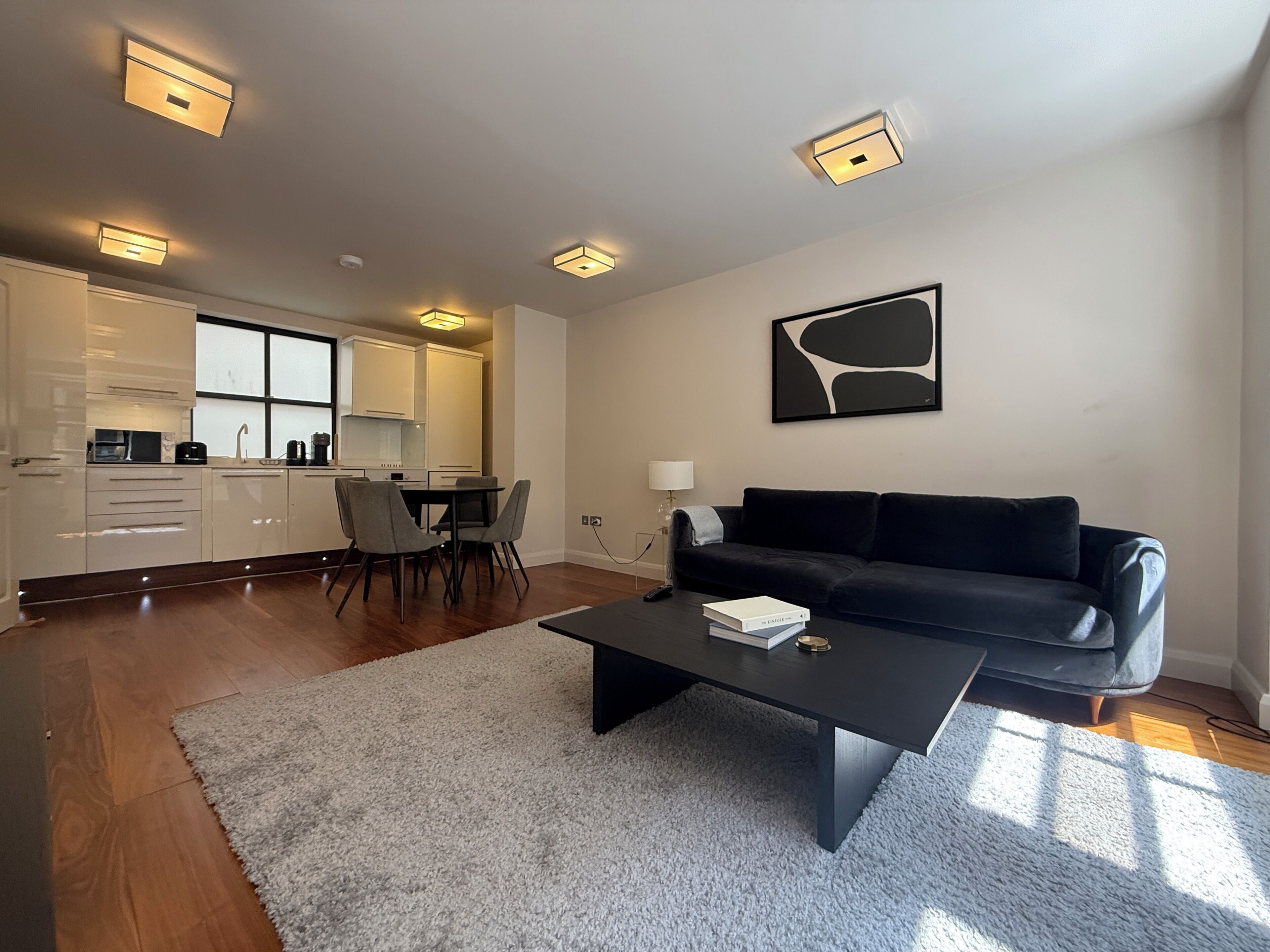 A modern living room with a dark sofa, a coffee table, and a kitchen in the background.