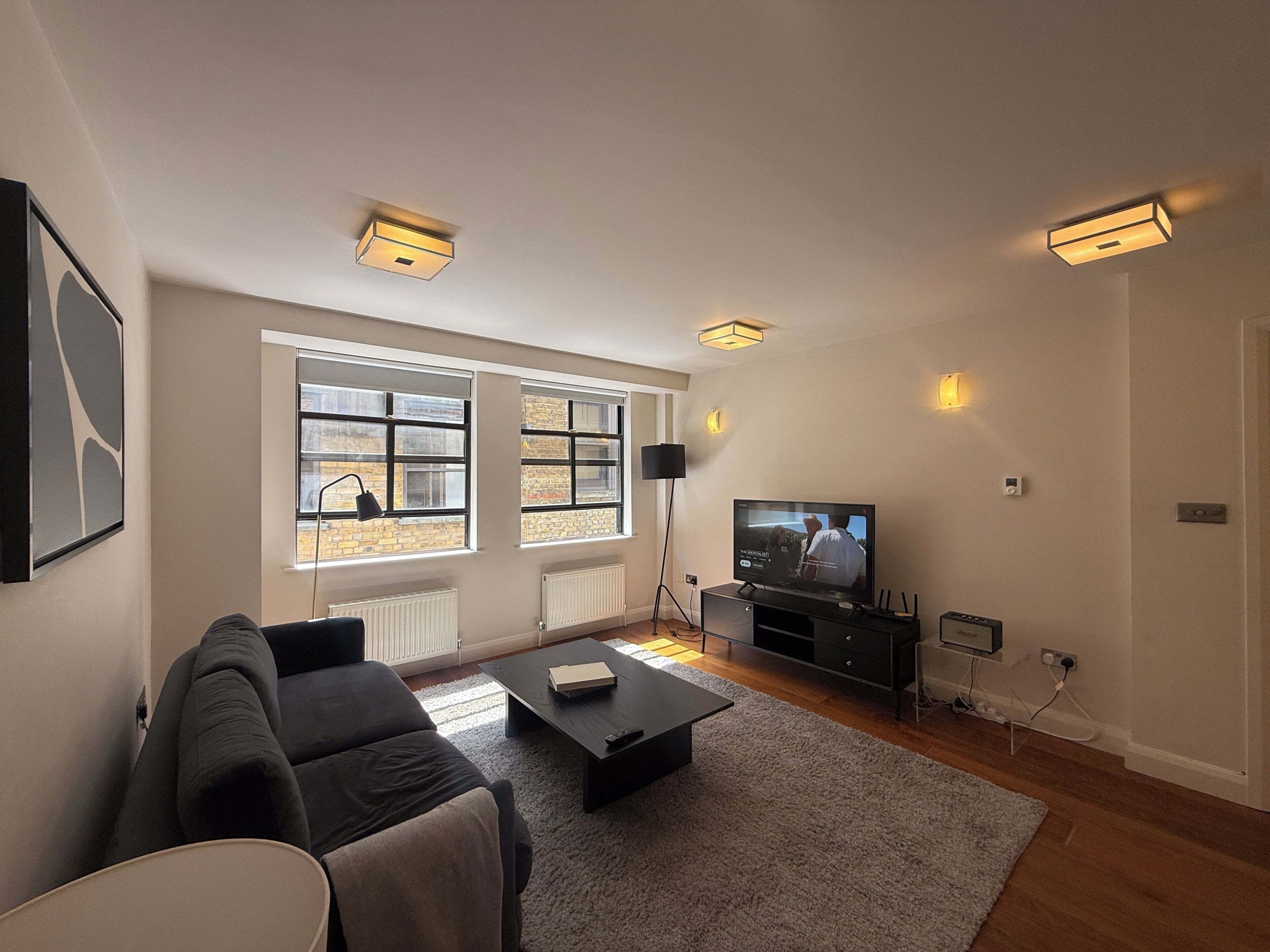 A modern living room with a sofa, coffee table, TV, and large windows.
