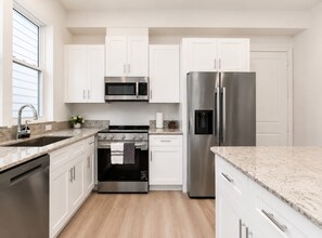 A modern kitchen with white cabinets, stainless steel appliances, and a granite countertop. - Modern 3BR, Garage & Yard, Near Downtown Houston (Houston)