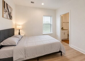 A bedroom with a bed, bedside lamp, and a window with blinds. - Modern 3BR, Garage & Yard, Near Downtown Houston (Houston)