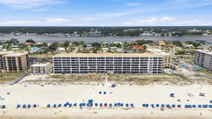 Ein Hotel direkt am Strand mit mehreren Etagen, ein Sandstrand davor und Blick auf das Wasser und die Skyline im Hintergrund.
