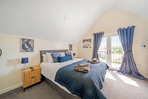 A bedroom with a bed, a nightstand, a lamp, and a view of the outdoors through a door. - Lodge 4 - Pavilion (Brigg)