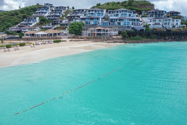 Un hotel costero con varias edificaciones, una playa de arena y un mar turquesa transparente.