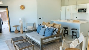 Una sala de estar moderna con sofá, mesa de centro y sillas, una cocina con microondas y un comedor con taburetes.