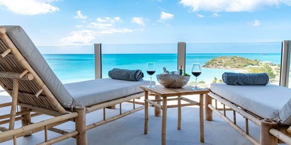 A wooden deck with two lounge chairs and a table, overlooking a turquoise sea and a distant island. - Spacious Antigua Suite with Infinity Pool & Wraparound Terrace (Urlings)
