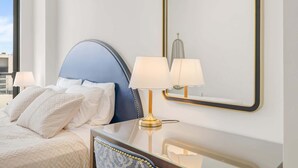 Et hotelværelse med en seng, to sengeborde med lamper, et spejl og udsigt over byen.