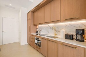 A modern kitchen with wooden cabinets, a marble countertop, a built-in oven, a coffee maker, and a sink. - Chic Miami Apt Pool, Gym & Sleeps 4 (Miami)