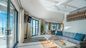 Un vaste espace de vie comprenant un canapé, une table basse et une table à manger. De grandes fenêtres laissent entrer beaucoup de lumière naturelle et offrent une vue sur l’extérieur.
