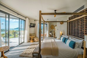 Un dormitorio espacioso con una cama grande, dosel de madera, vista al mar, balcón con asientos y televisor.