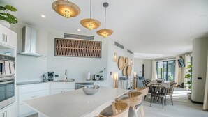 A modern kitchen with white cabinetry, a large island, and wooden chairs. - Seastar: Luxury 2-Bedroom Ocean-View Suite with Private Pool, Antigua (Urlings)