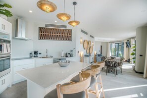 A modern kitchen with white cabinetry, a large island, and wooden chairs. - Seastar: Luxury 2-Bedroom Ocean-View Suite with Private Pool, Antigua (Urlings)