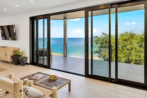 Una sala de estar moderna con un amplio ventanal corredero que da a un balcón con vistas al mar.
