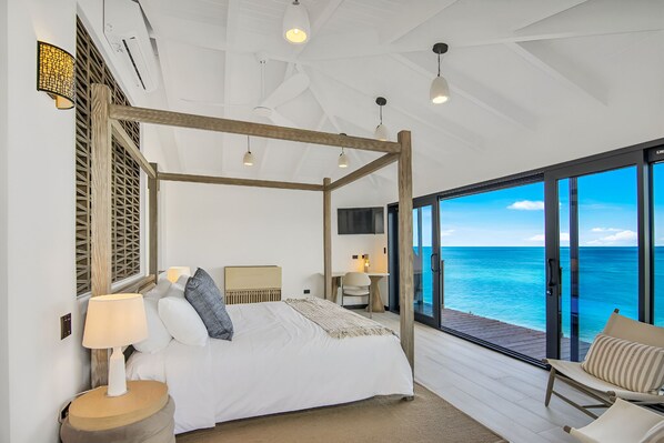 Un dormitorio con cama con dosel, un escritorio, una silla y vista al océano.