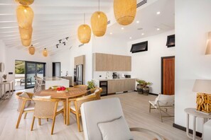 Una cocina moderna con armarios de madera, un comedor con sillas de mimbre y un amplio ventanal con vistas a la vegetación.