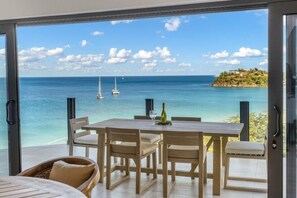 Un comedor con una mesa y sillas, una botella de champán y vistas al mar con barcos.