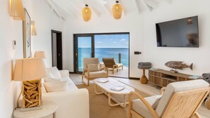 Una sala de estar moderna con televisor grande, asientos cómodos y vista al océano.